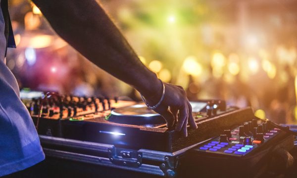 Dj mixing outdoor at beach party festival with crowd of people i Dj mixing outdoor at beach party festival with crowd of people in background - Summer nightlife view of disco club outside - Soft focus on hand - Fun ,youth,entertainment and fest concept